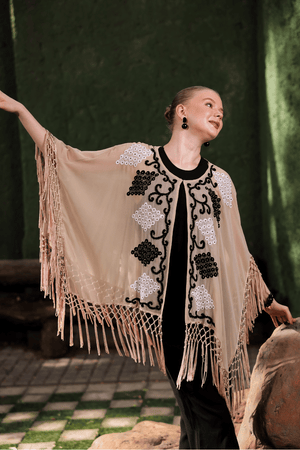 Model in motion wearing beige cape – showcasing fringe movement and sheer texture