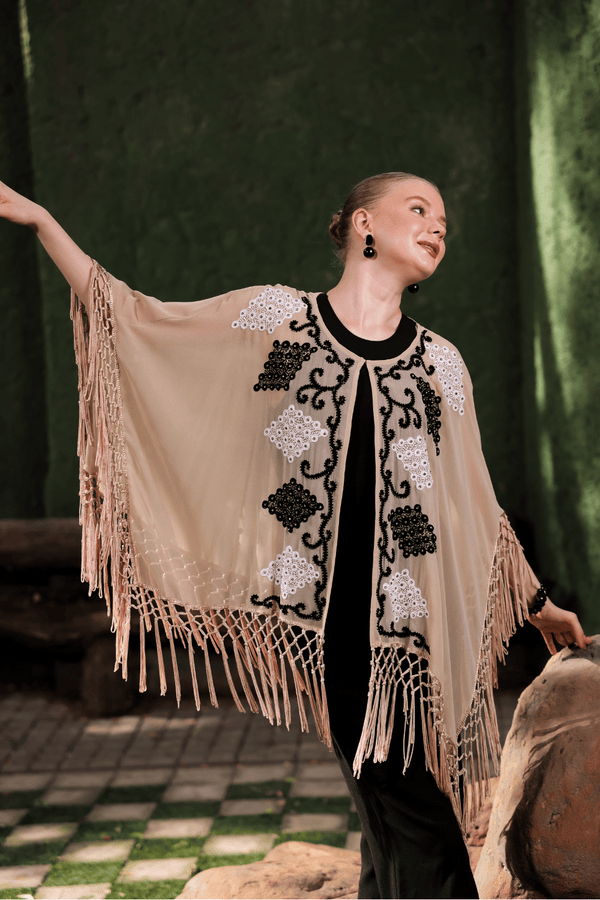 Model in motion wearing beige cape – showcasing fringe movement and sheer texture