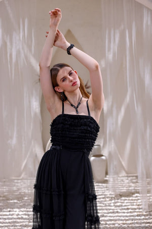 Woman in a black dress posing with arms raised against a textured wall.