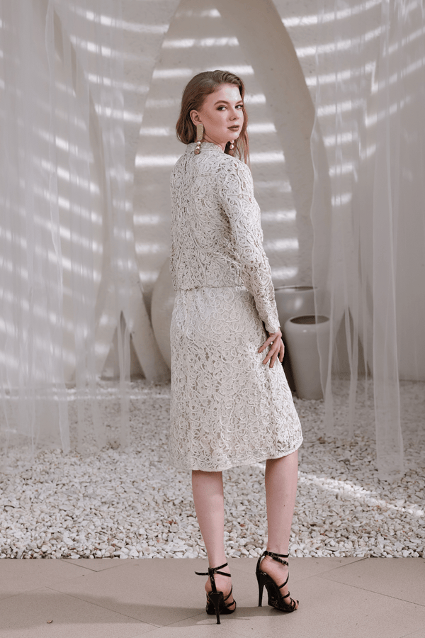 Back view of model wearing ivory hand-beaded lace shrug and matching dress in natural light