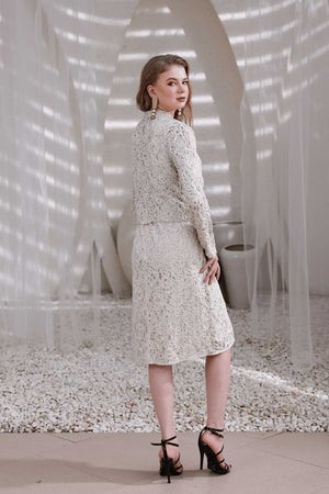 Back view of model wearing ivory hand-beaded lace shrug and matching dress in natural light